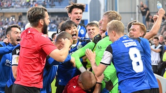 Spieler und Verantwortliche von Arminia Bielefeld feiern Torhüter Jonas Kersken (in grün) nach dem Spiel im DFB-Pokal gegen den VfL Bochum am 12. August 2023.