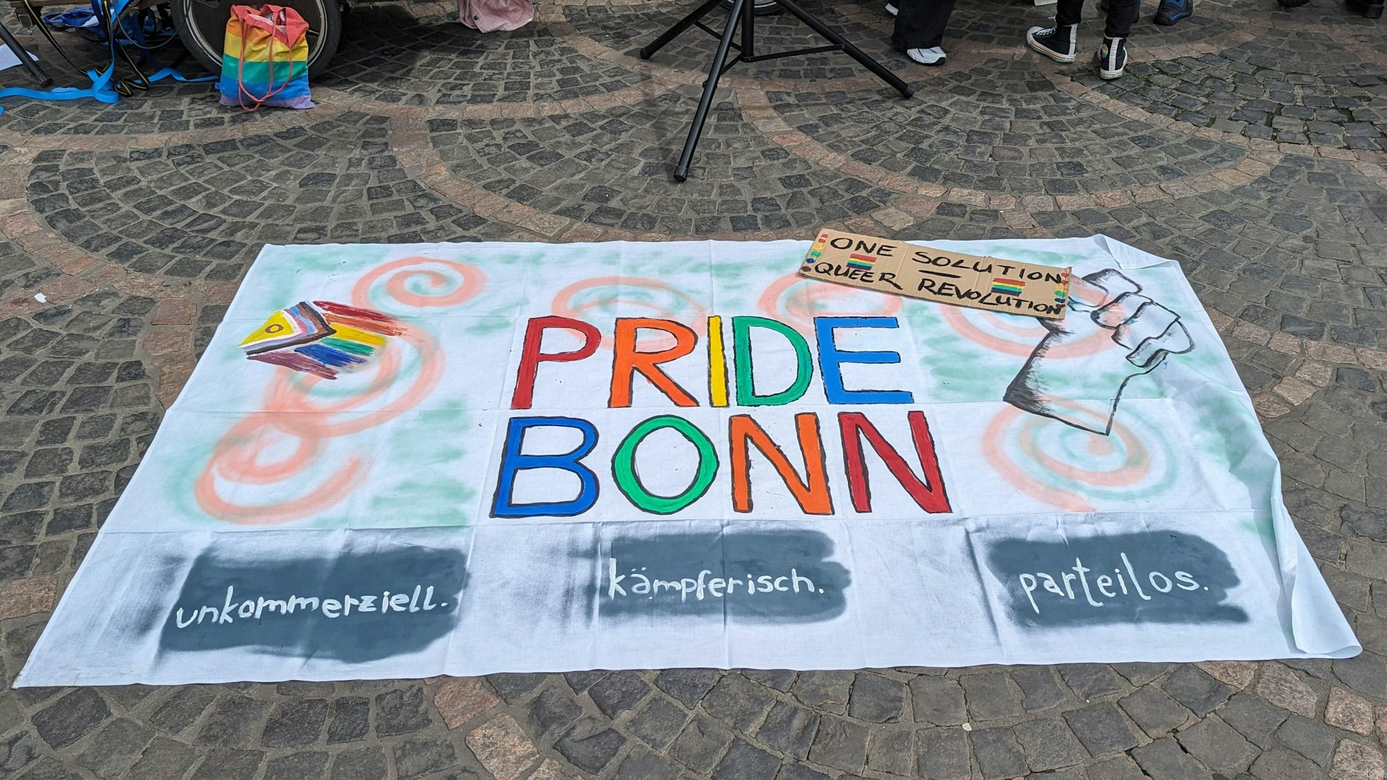 Das Banner der Pride Bonn liegt ausgebreitet auf dem Boden.