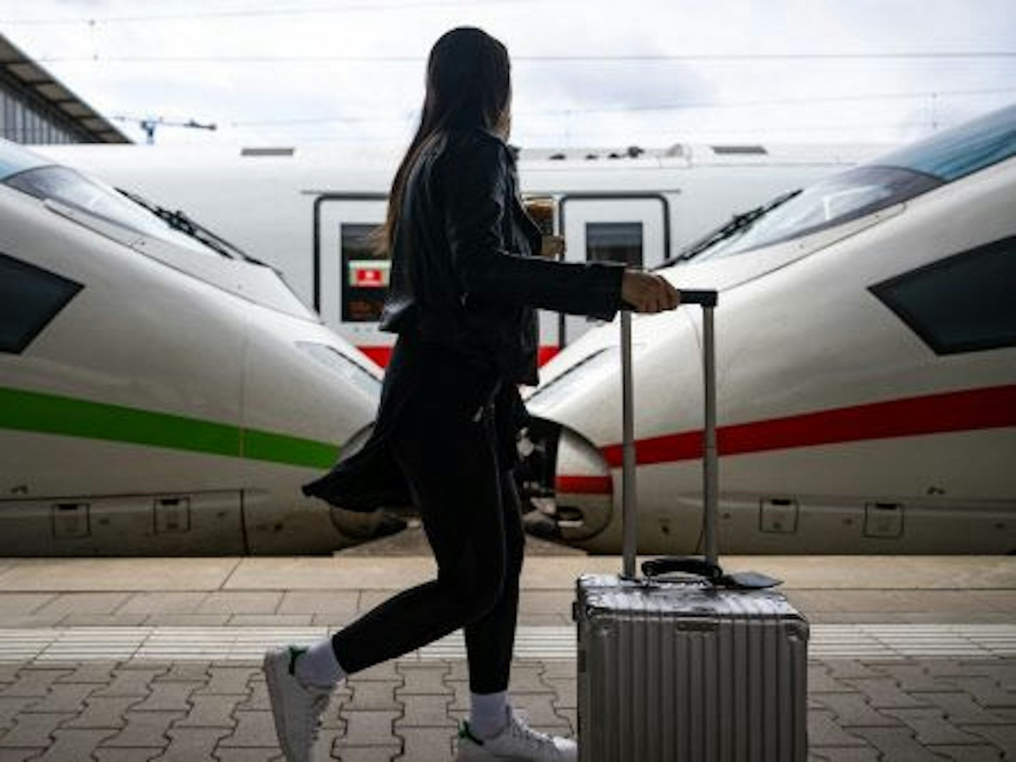 Eine Reisende geht am Hauptbahnhof in München an ICE-Zügen vorbei den Bahnsteig entlang.