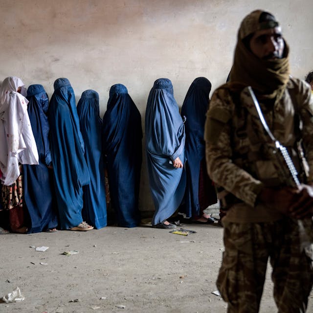 Afghanistan, Kabul: Ein Taliban-Kämpfer steht Wache, während Frauen darauf warten, von einer humanitären Hilfsorganisation verteilte Lebensmittelrationen zu erhalten.