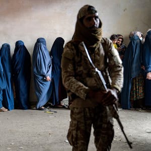 Afghanistan, Kabul: Ein Taliban-Kämpfer steht Wache, während Frauen darauf warten, von einer humanitären Hilfsorganisation verteilte Lebensmittelrationen zu erhalten.