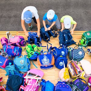 Drei Erstklässler stellen in einer Grundschule ihre Schultaschen ab.