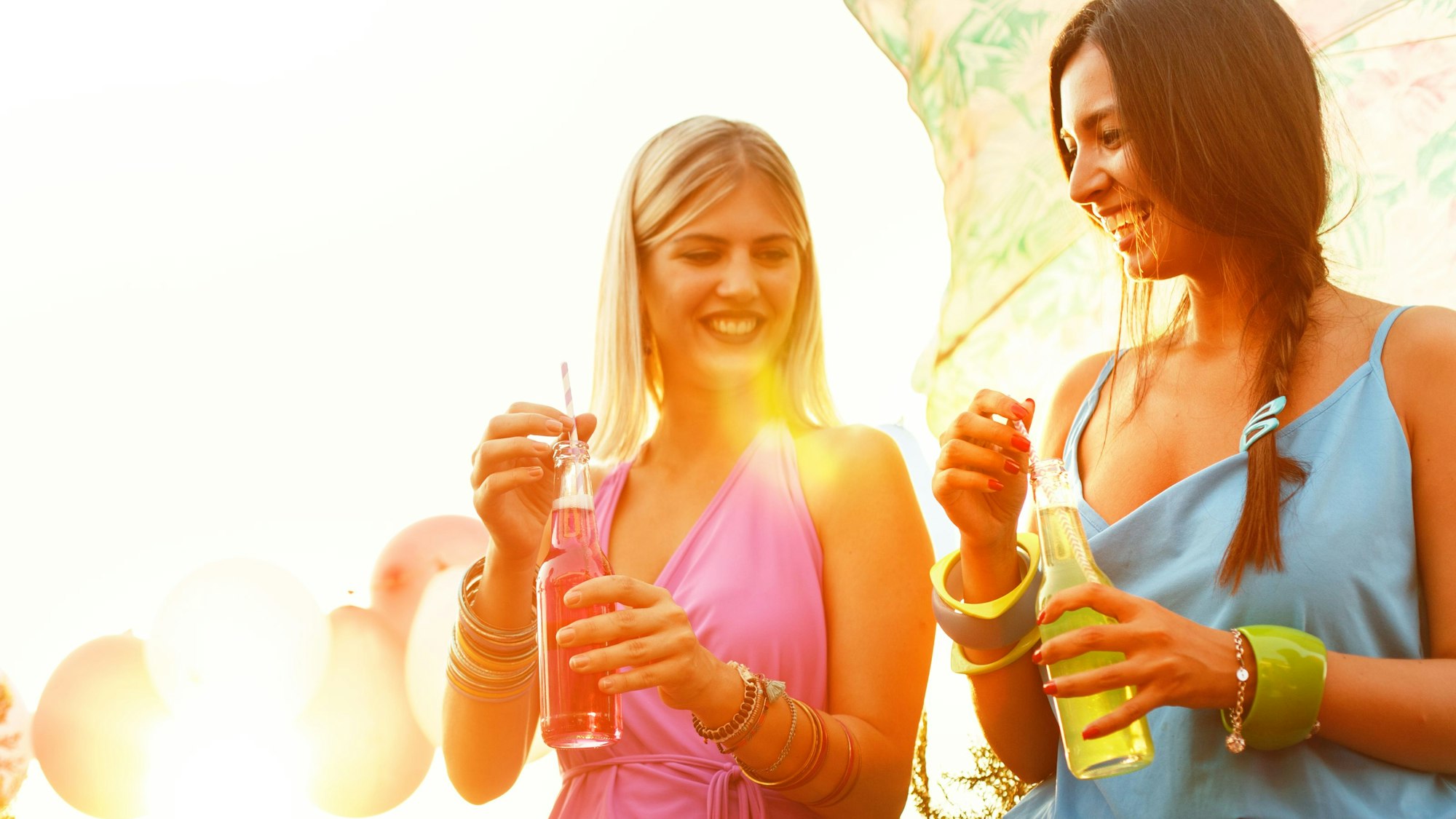 Zwei Frauen in Sommerkleidern trinken Limonade.