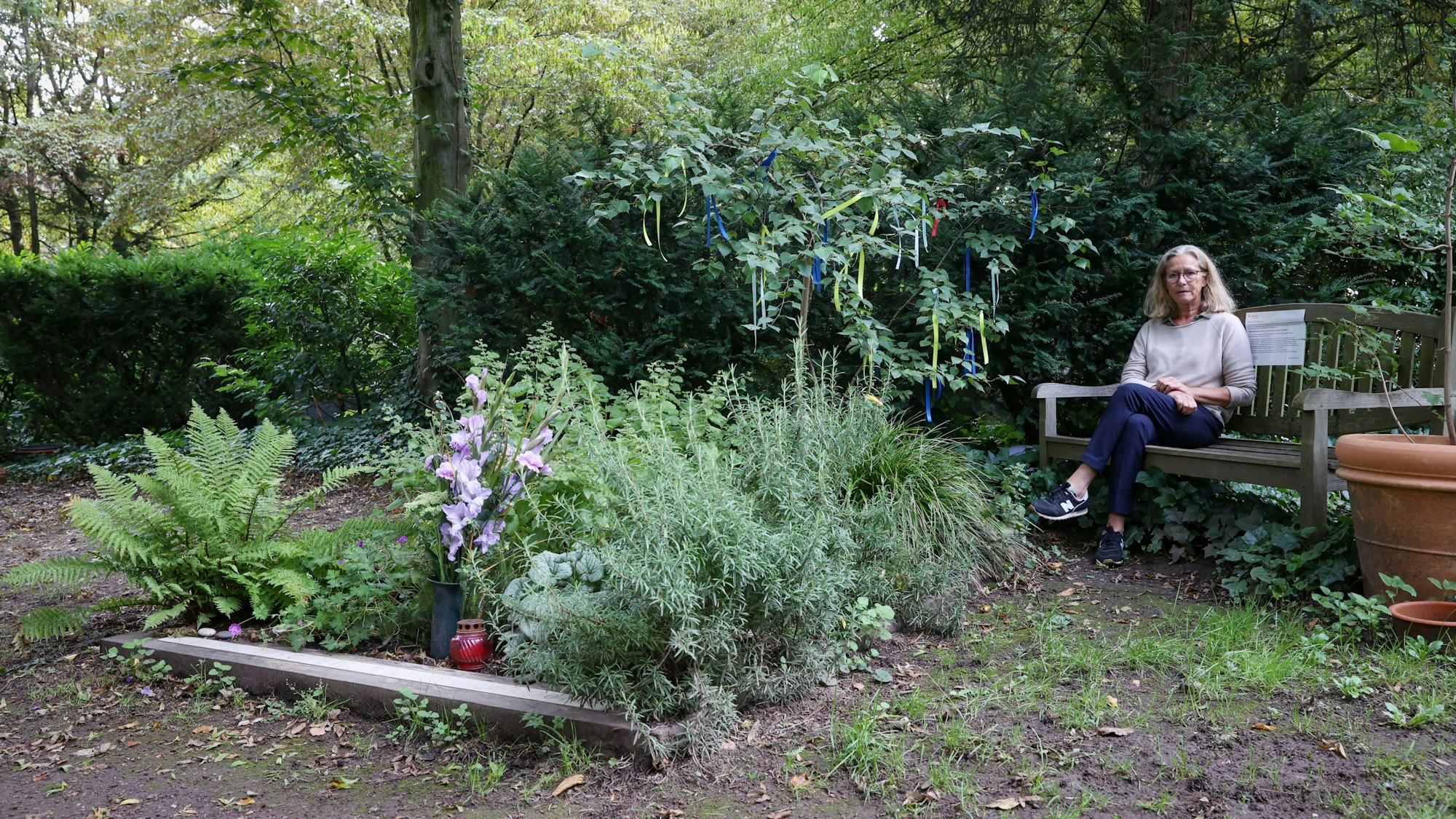 Annegret Fleischel sitzt auf einer Holzbank neben dem Grab ihres Sohnes auf dem Melatenfriedhof in Köln.