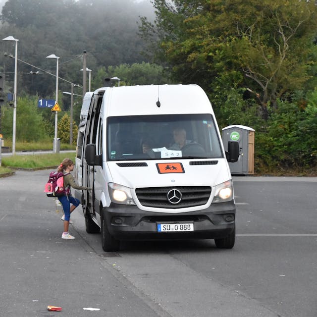 Kinder steigen in einen Kleinbus ein.