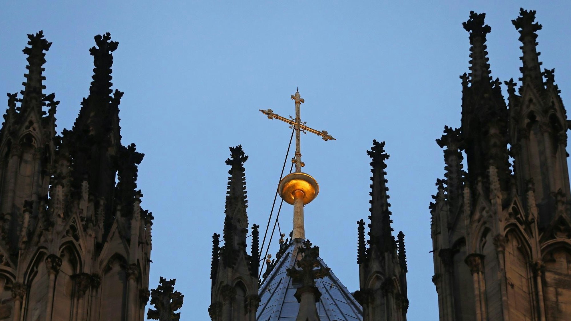 Zu sehen ist ein Kreuz steht hinter dem Strebewerk am Kölner Dom.