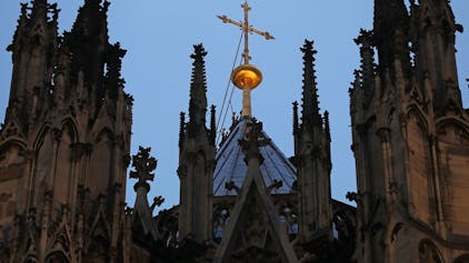Ein Kreuz steht hinter dem Strebewerk am Dom.