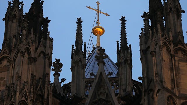 Zu sehen ist ein Kreuz steht hinter dem Strebewerk am Kölner Dom.&nbsp;