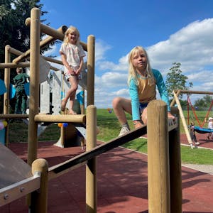 Zwei Mädchen klettern auf einem neuen Klettergerüst eines Spielplatzes.