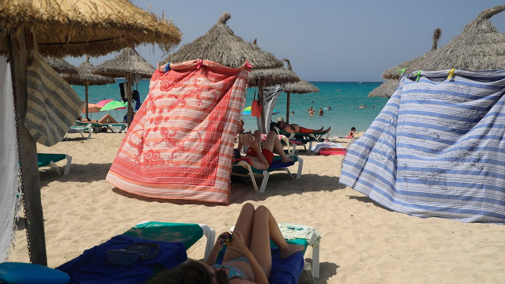 Menschen schützen sich bei hohen Temperaturen mit Strandtüchern vor der Sonne am Strand von Arenal.