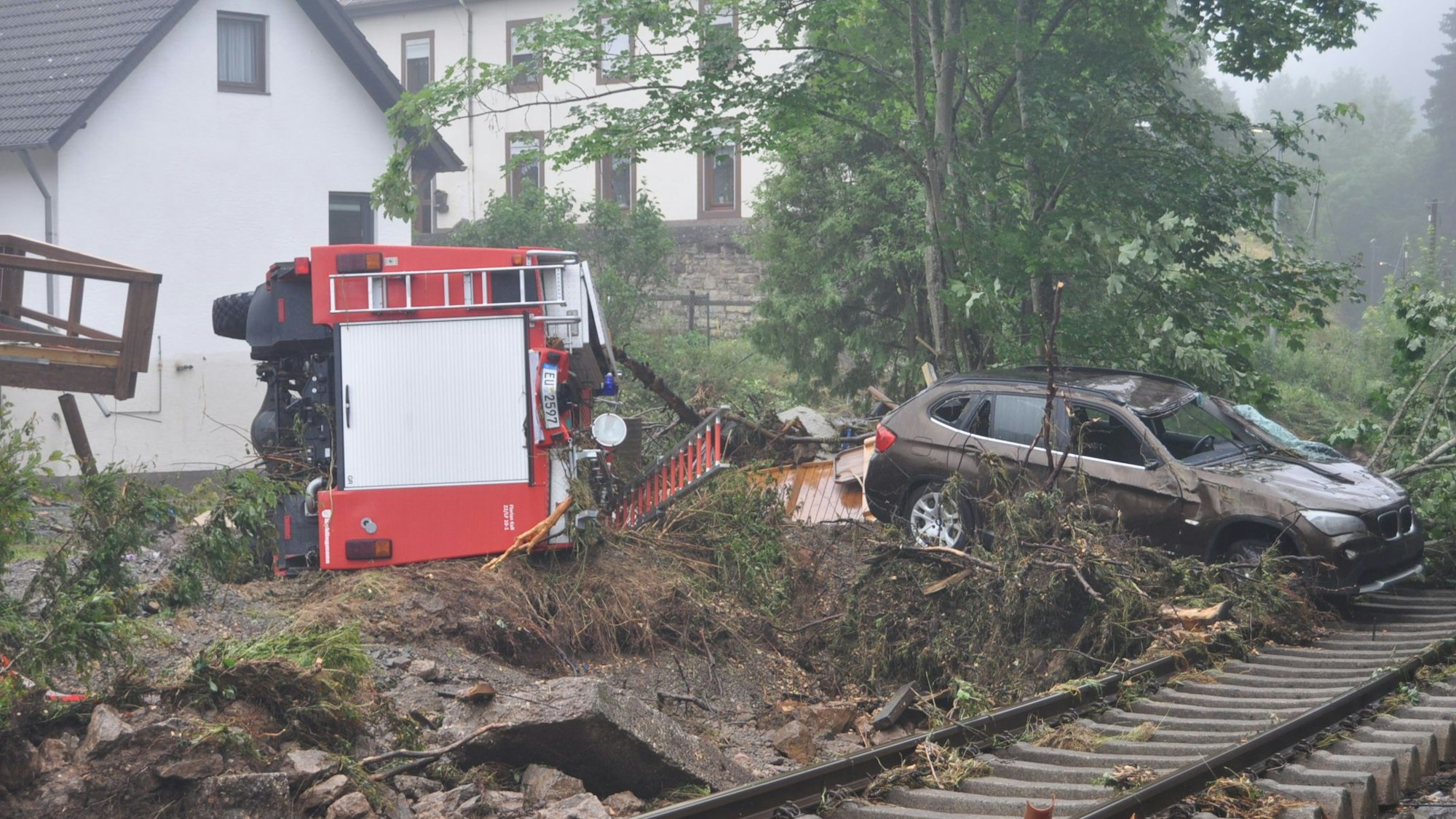 Das Bild zeigt das umgestürzte Fahrzeug der Löschgruppe Wahlen. Es liegt hinter den Gleisen inmitten der Verwüstung, die die Flut hinterließ.