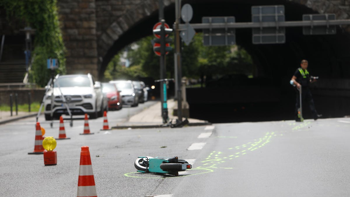 Ein kaputter E-Scooter liegt auf der Straße in Köln. Daneben sind Absperrungen der Polizei zu sehen.