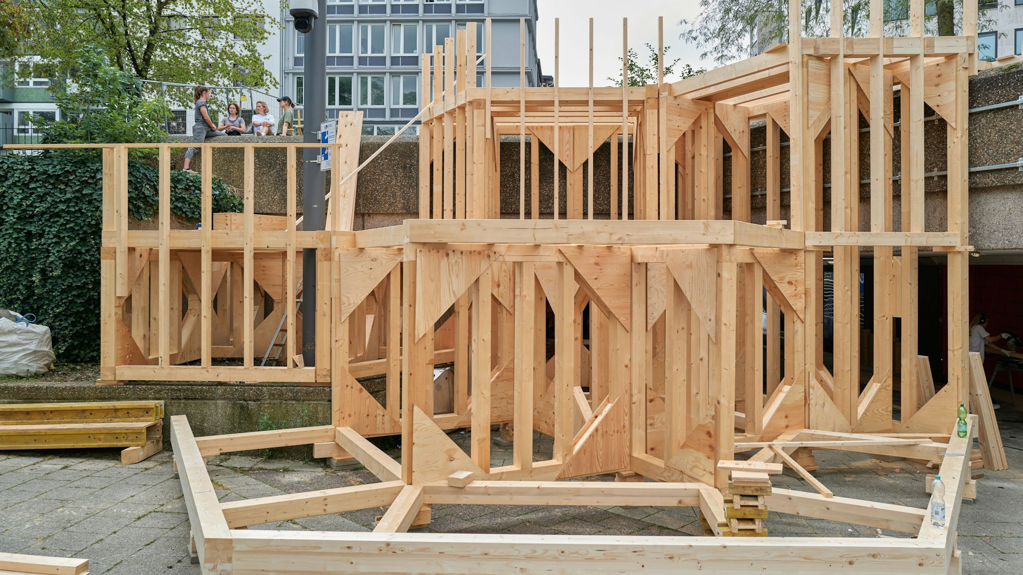 Handwerkerinnen und Handwerker bauen das Grundgerüst für die Freitreppe, die übergangsweise am Ebertplatz entsteht. Es ist ein großes Gerüst aus Holz.