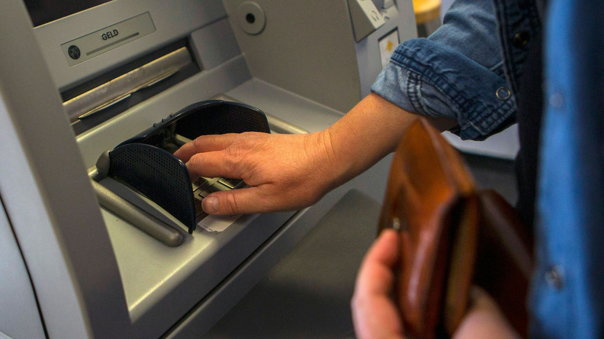 Eine Person gibt ihre PIN-Nummer beim Geldabheben an einem Geldautomaten ein.