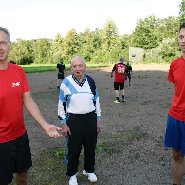 Drei Männer aus drei Familiengenerationen stehen auf einem Sportplatz nebeneinander: Vater, Sohn und Enkel.