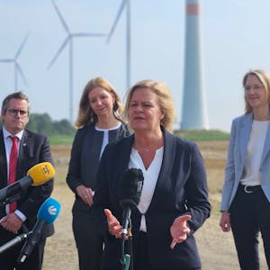 Bundesinnenministerin Nancy Faeser spricht vor Windrädern bei einem Pressetermin in Mikrophone. Hinter ihr stehen Bedburgs Bürgermeister Sascha Solbach und zwei Frauen von RWE.