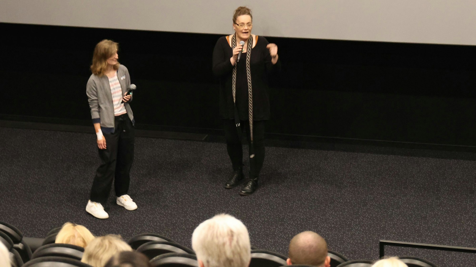 In einem der Säle des Gummersbacher Kinocenters Seven stehen Marie Brück (r.) und Moderatorin Nadine Lindörfer vom Netzwerk gegen Rechts vor der dunklen Leinwand und sprechen über Brücks langen und schmerzhaften Weg vom Mann zur Frau.
