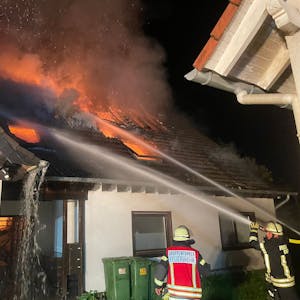Feuerwehrleute löschen mit Wasser die Flammen, die aus dem Dach eines Hauses schlagen.