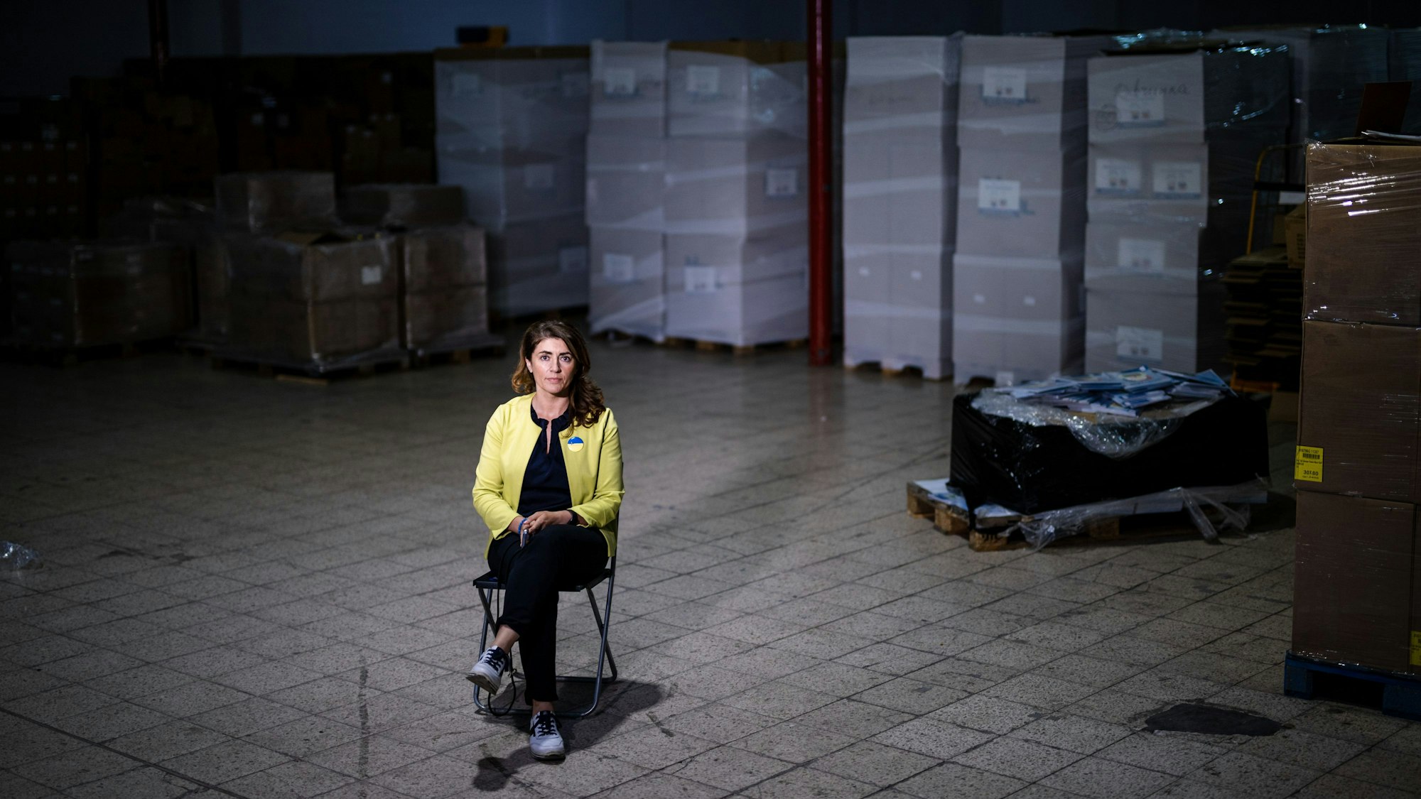 Eine Frau sitzt in einer Halle vor Paletten mit Hilfsgütern.