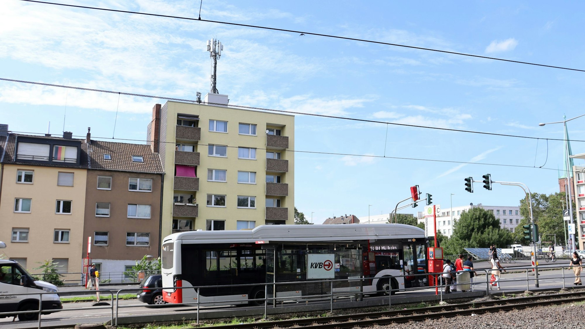 Eine Mobilfunk-Antenne auf einem mehrstöckigen Gebäude ist zu sehen, davor eine mehrspurige Straße mit einem Bus und Straßenbahnschienen.