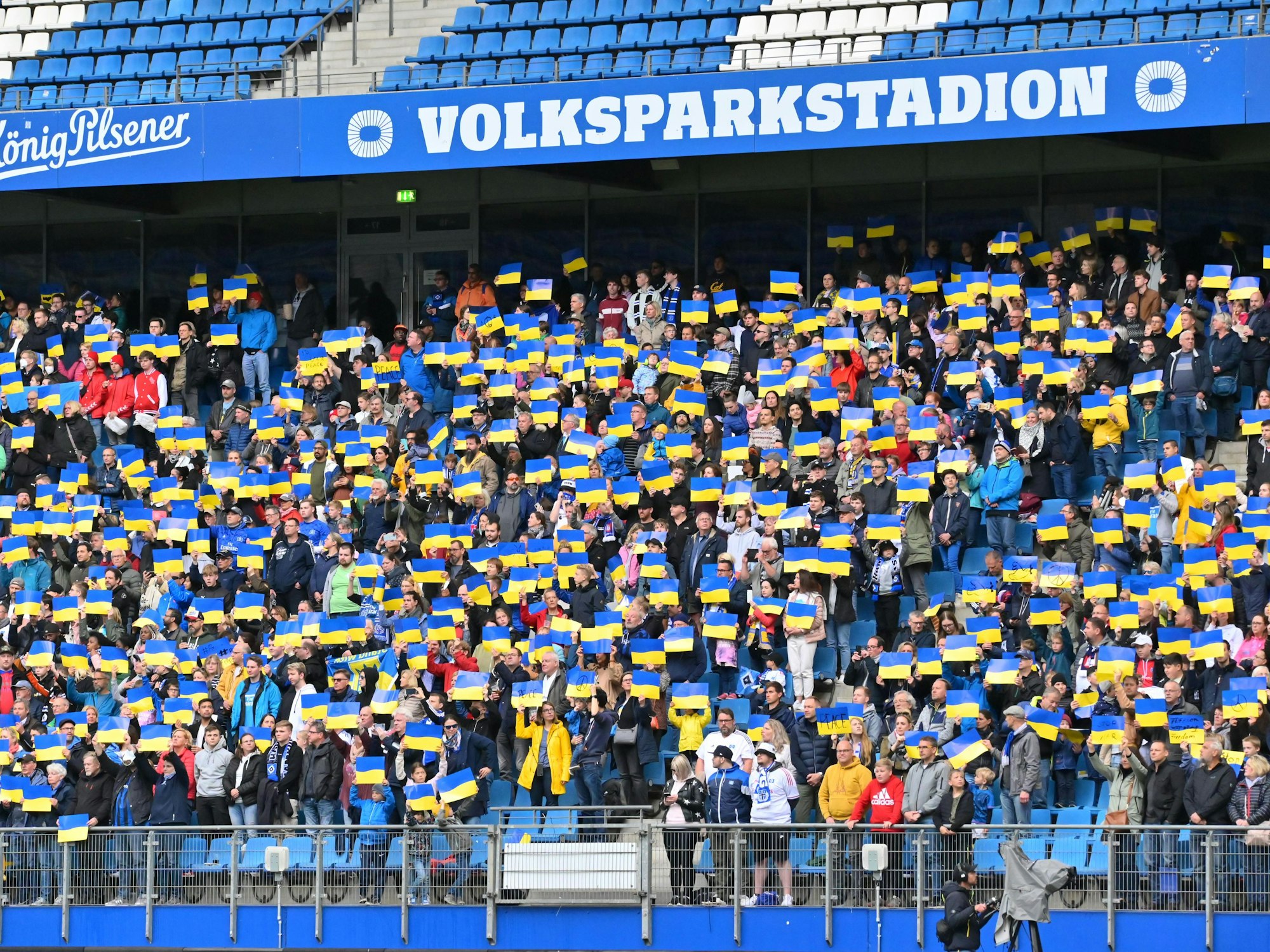 Die Zuschauer des Benefizspiels am 28. Mai 2022 stehen auf ihren Plätzen und halten Plakate mit der ukrainischen Fahne in die Höhe, während die ukrainische Nationalhymne gespielt wird.