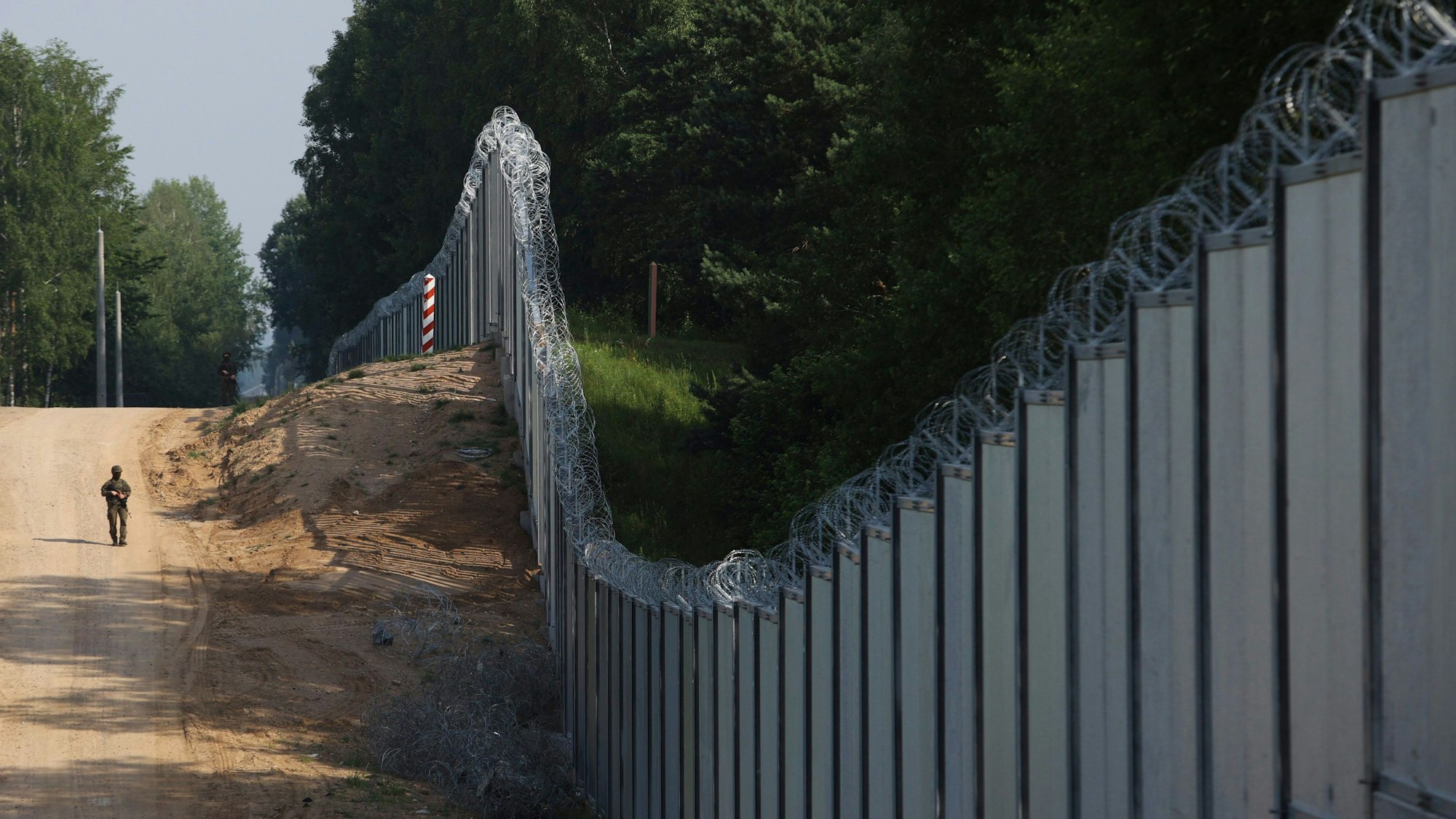 Ein polnischer Grenzschutzbeamter patrouilliert im Bereich einer errichteten Metallmauer an der Grenze zwischen Polen und Belarus, die mit Stacheldraht versehen ist.