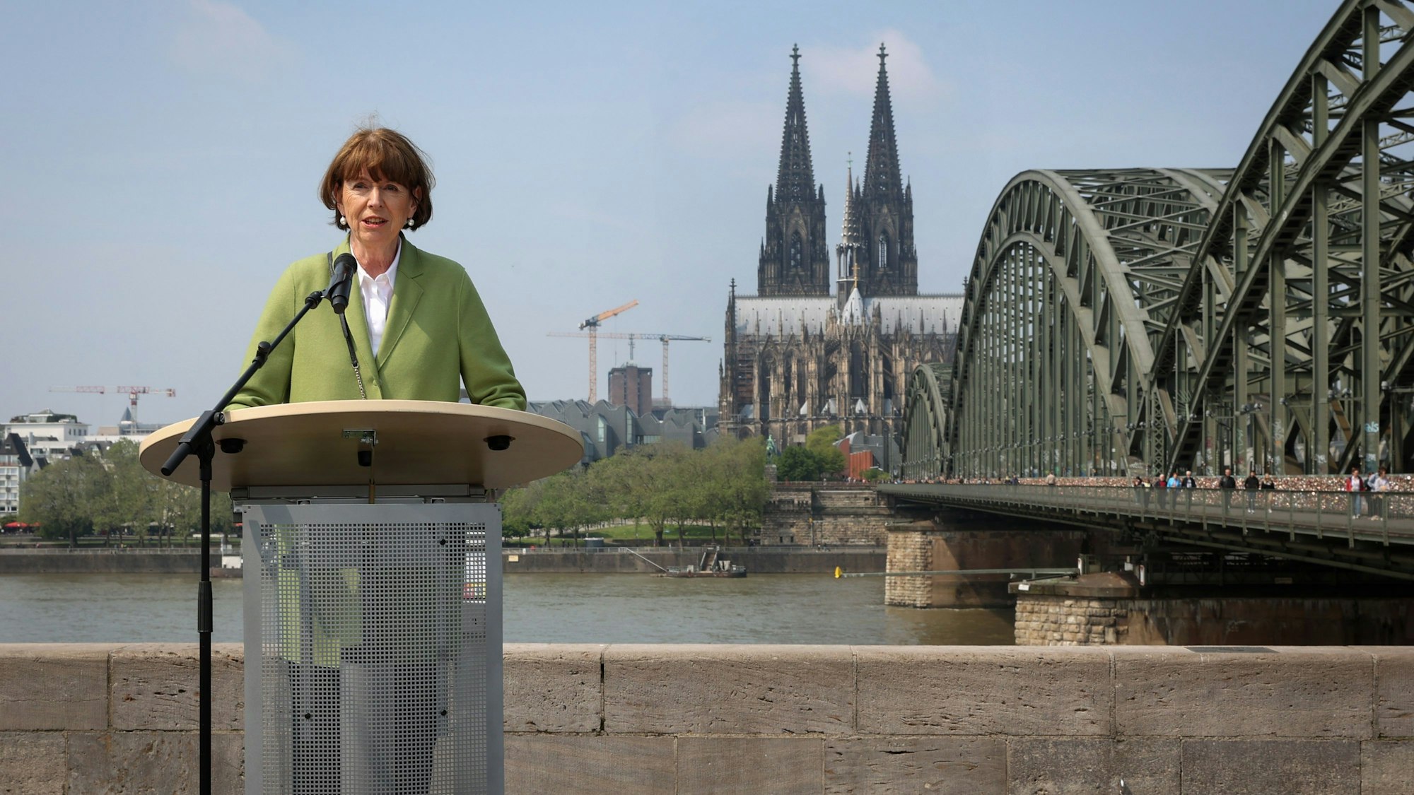 Oberbürgermeisterin Henriette steht am Rhein mit dem Kölner Dom im Hintergrund.