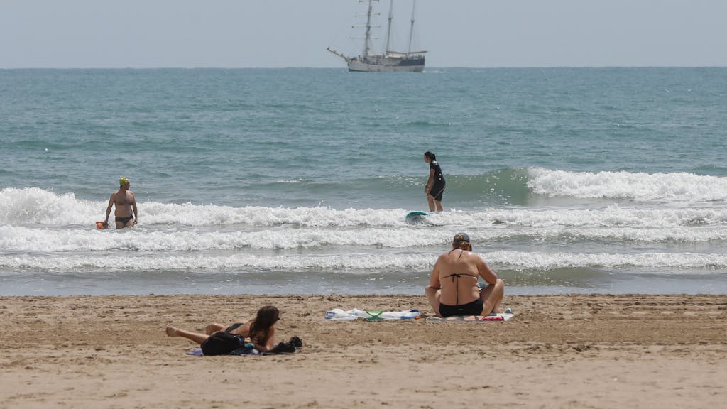 Mehrere Personen baden und sonnen sich an einem Strand in Valencia.