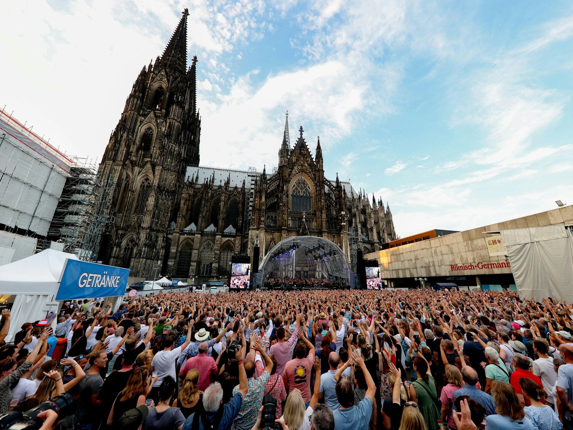 Viele Menschen stehen vor der Kulisse des Kölner Doms, im Hintergrund ist die Bühne von Brings zu sehen.