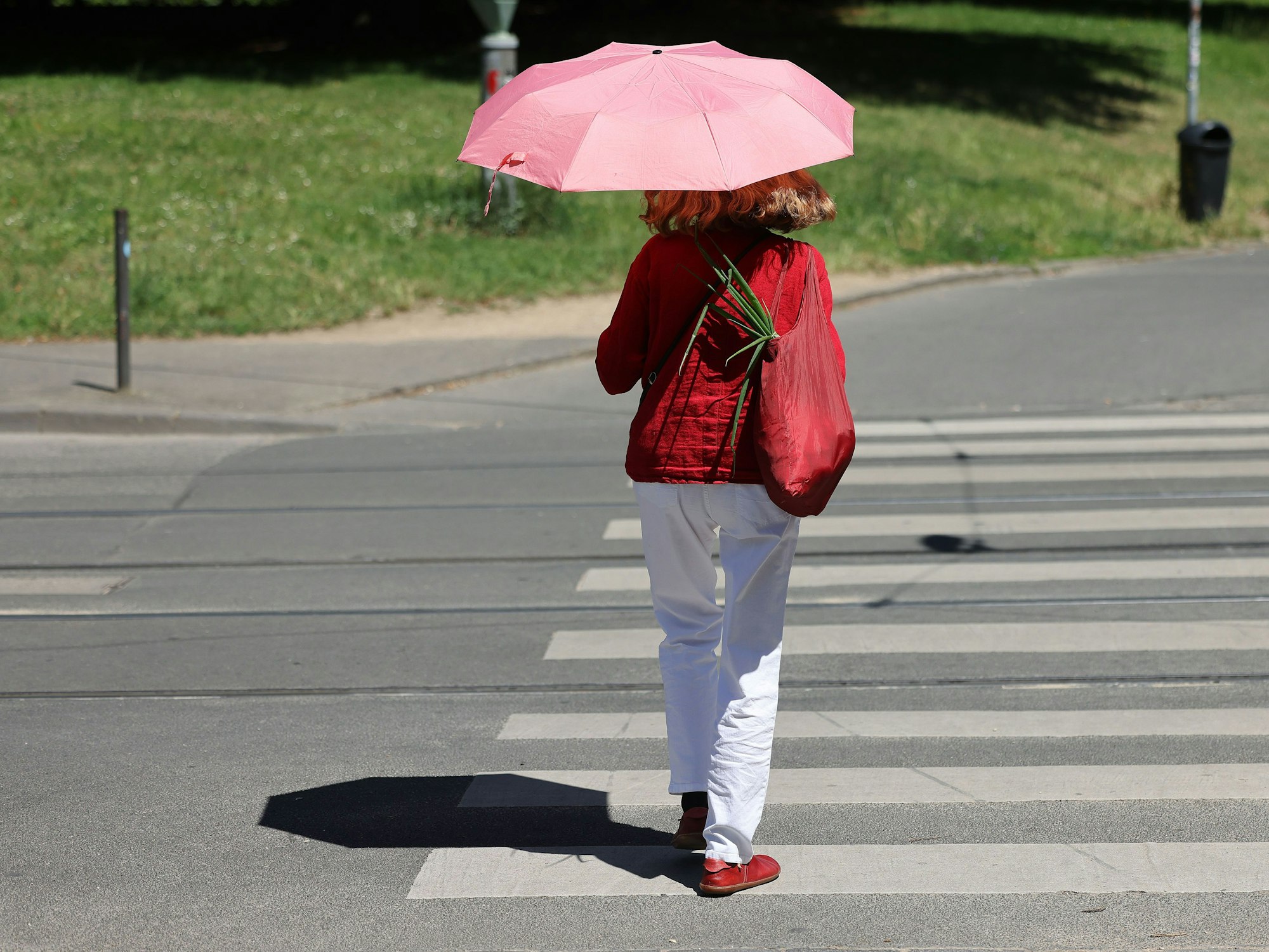 Eine Frau geht mit einem Regenschirm als Sonnenschirm durch Bonn: In Teilen von NRW warnt der Wetterdienst am Samstag vor Hitze.