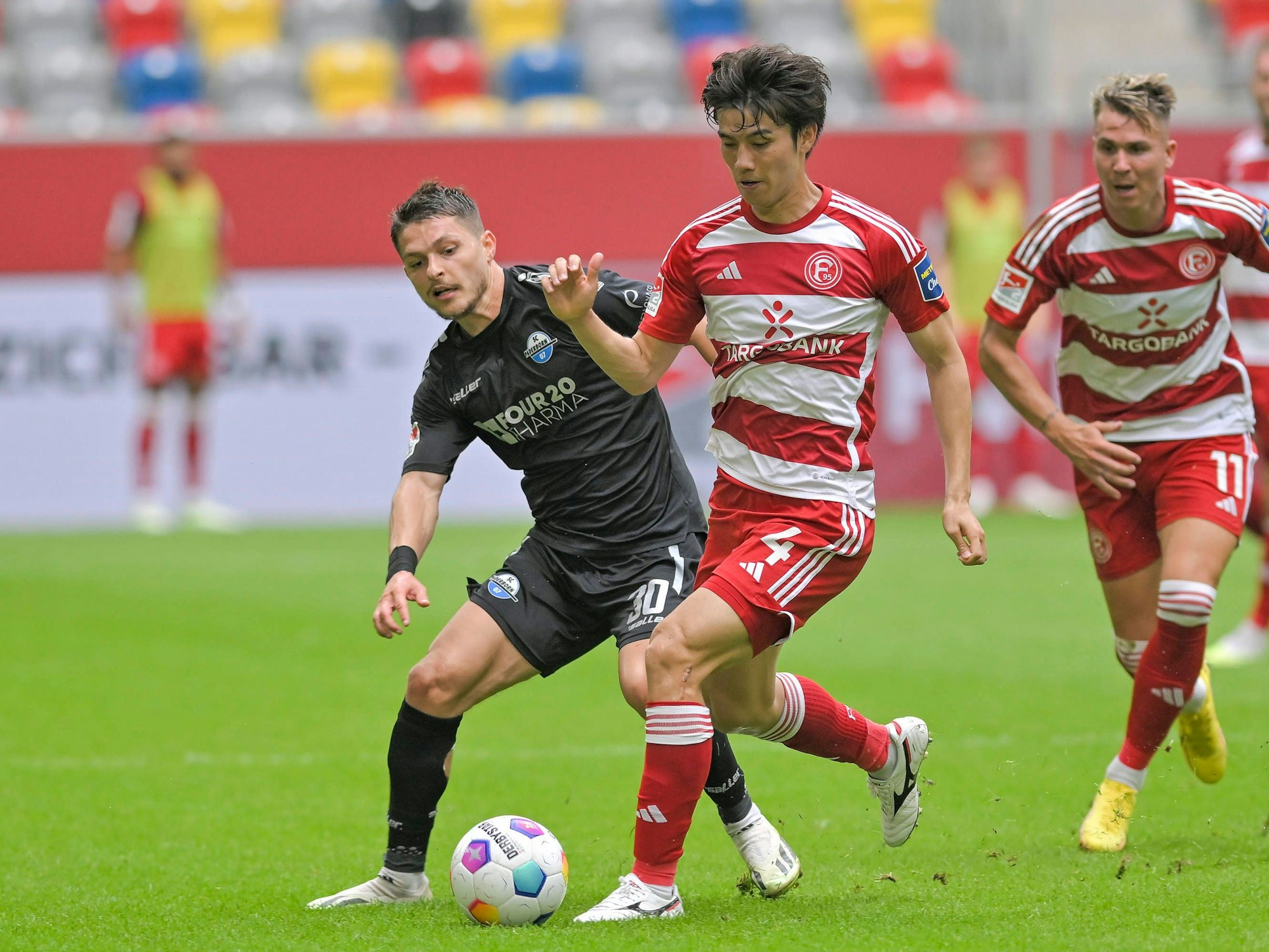 Ao Tanaka führt den Ball im Spiel gegen den SC Paderborn, er wird verfolgt von Florent Muslija.