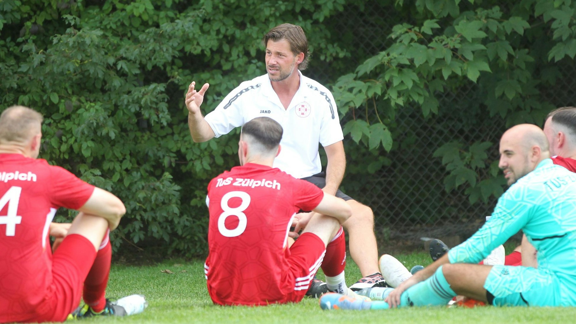 Zülpich-II-Trainer Marc Altendorf hält knieend eine Ansprache. Seine Spieler sitzen um ihn herum.