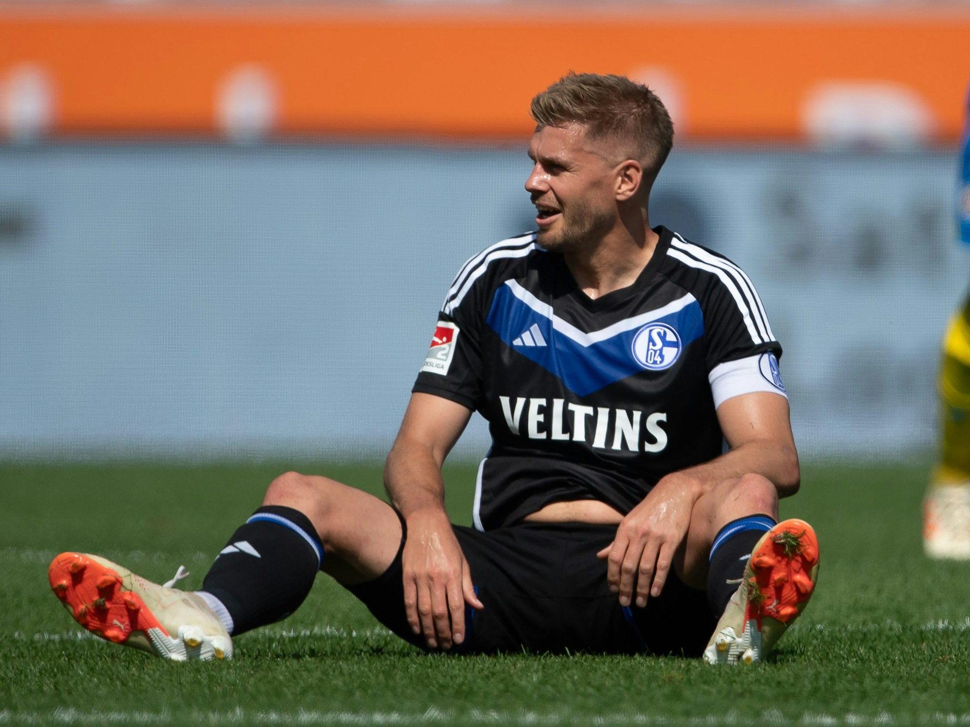 Simon Terodde sitzt im Schalke-Trikot auf dem Rasen.