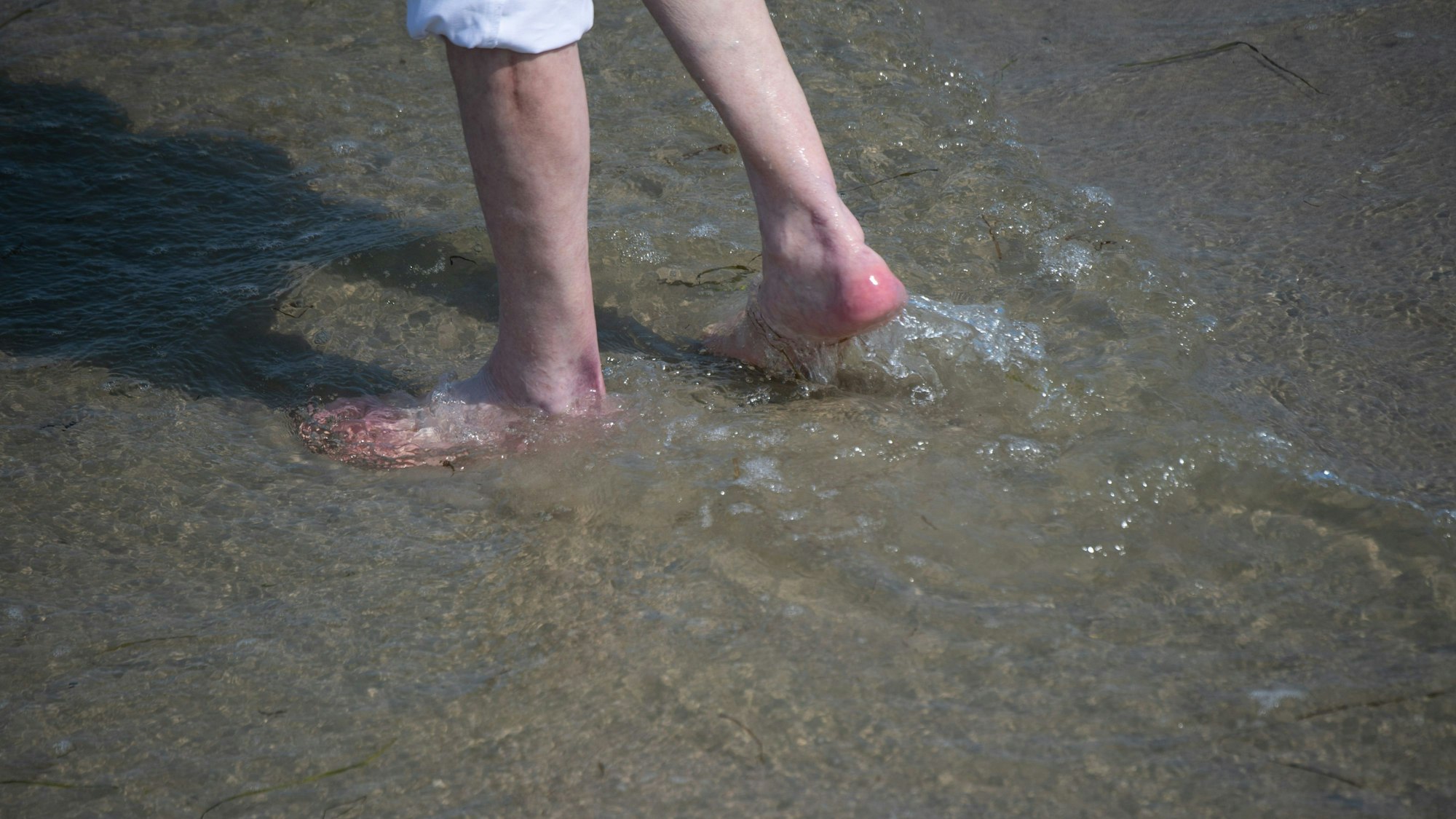 Ein Mann watet durch das flache Wasser an einem Ostsee-Strand. Die Meerwasser-Keime Vibrionen siedeln sich besonders häufig in flachem, stehendem Wasser an.