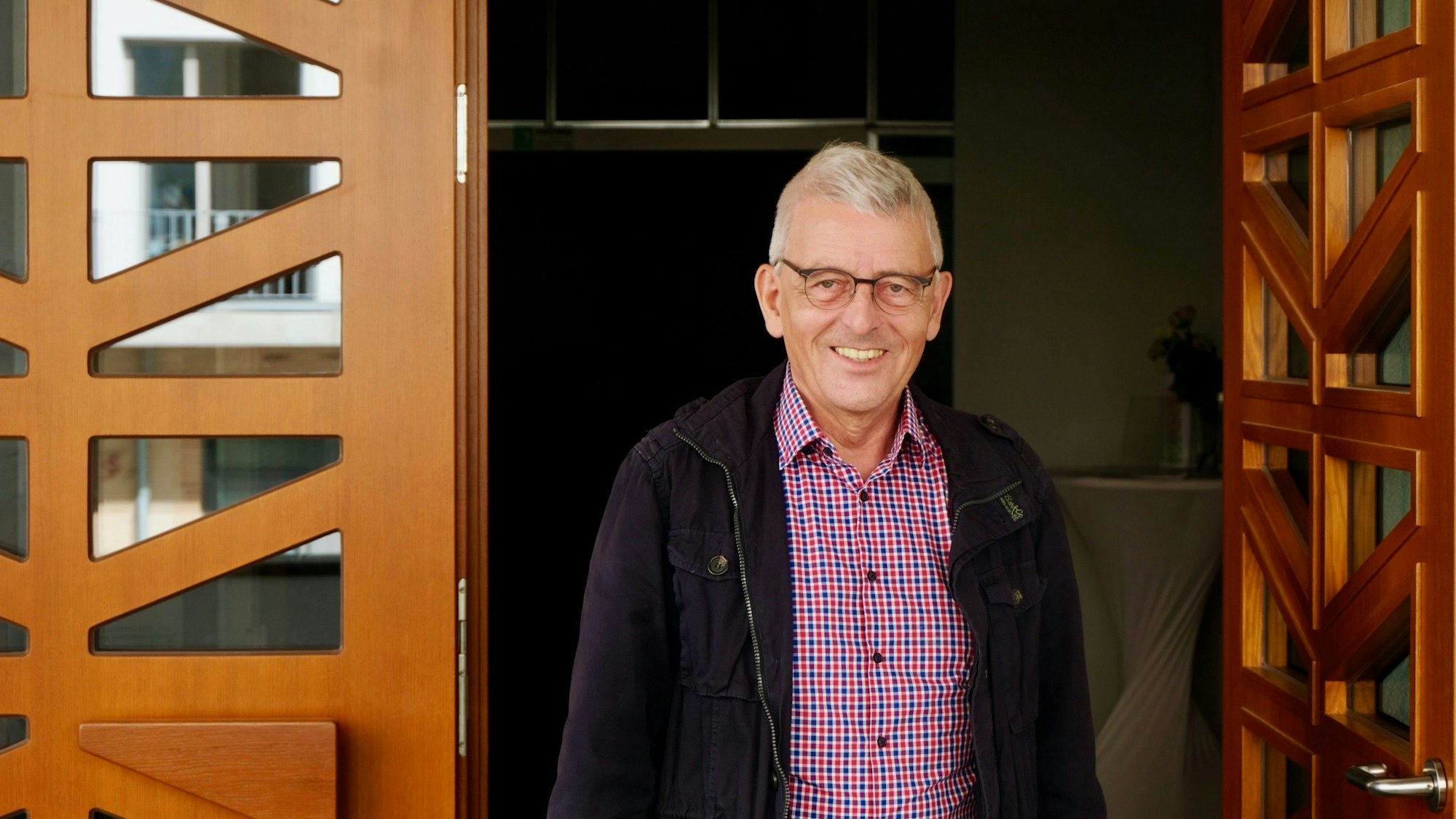 Ein Mann mit kurzem grauen Haar und Brille steht in einer geöffneten Kirchentür.