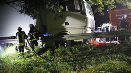 Nach dem Zusammenstoß eines Autos mit einem Pkw auf der A 3 kurz vor dem Ein weißer Lkw steht auf der Autobahn an einer Leitplanke, das Cockpit drückt die Leitplanke zur Seite. Feuerwehrleute stehen mit einem Schlauch daneben.