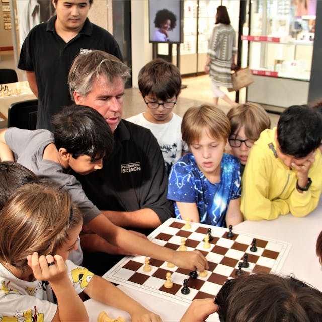 Der Profi Sebastian Siebrecht spielt Schach, um ihn herum stehen viele Kinder.
