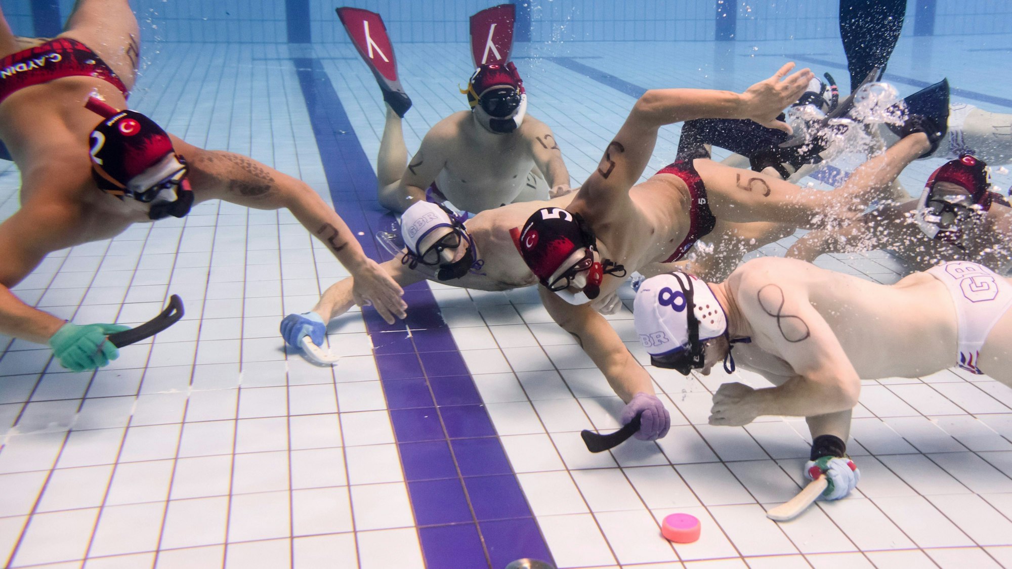 Spieler der türkischen und der deutschen Unterwasser-Hockey-Mannschaften spielen am Boden eines Schwimmbeckens