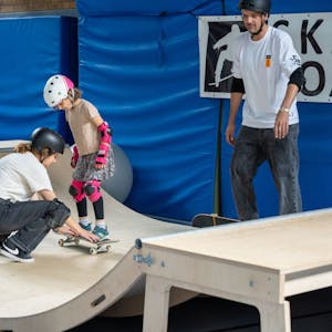 Eine Frau korrigiert den Stand eines Mädchens auf ihrem Skateboard.