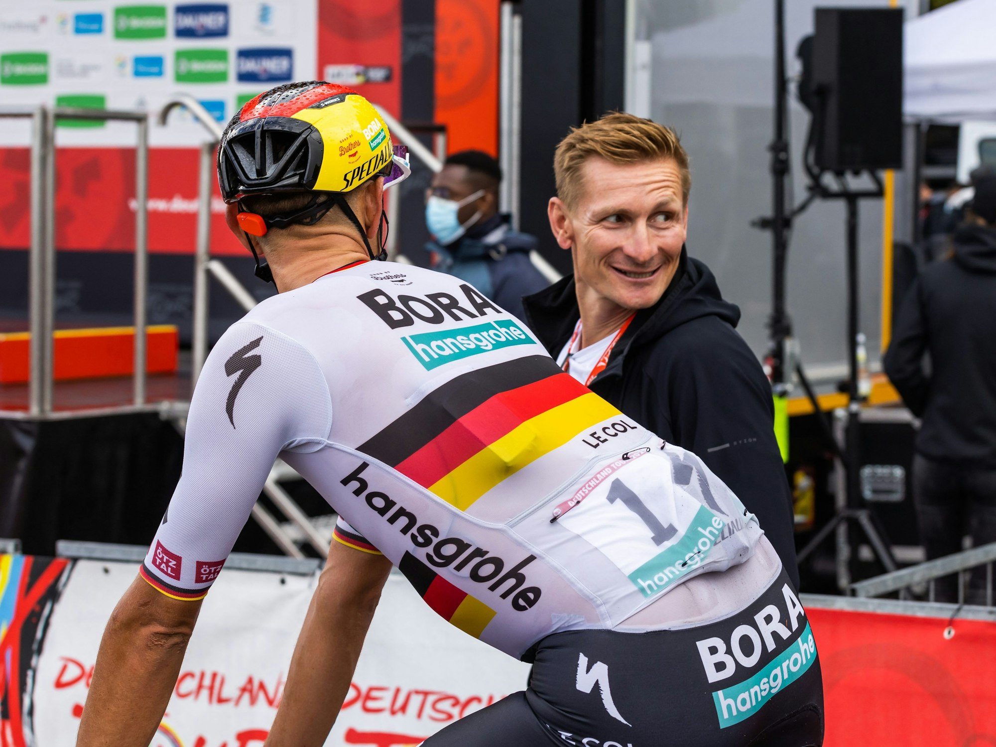 Nils Politt vom Team Bora-Hansgrohe (vorne) im Zielbereich mit dem ehemaligen Radprofi Andre Greipel.