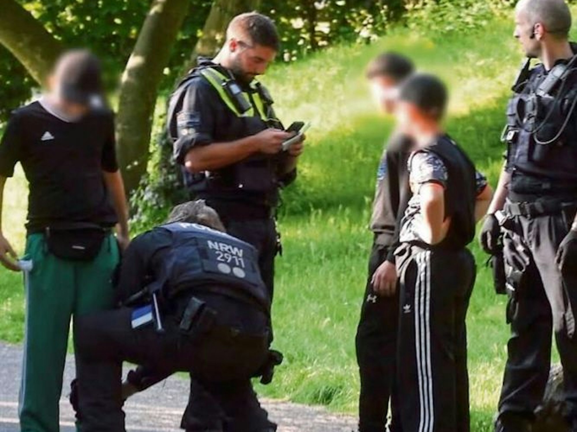 Polizisten durchsuchen drei Kinder von Kopf bis Fuß im Mülheimer Stadtpark.