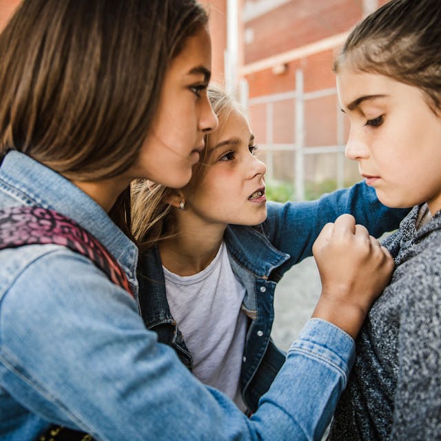 Ein Mädchen wird von zwei Schülerinnen auf dem Schulhof bedrängt.