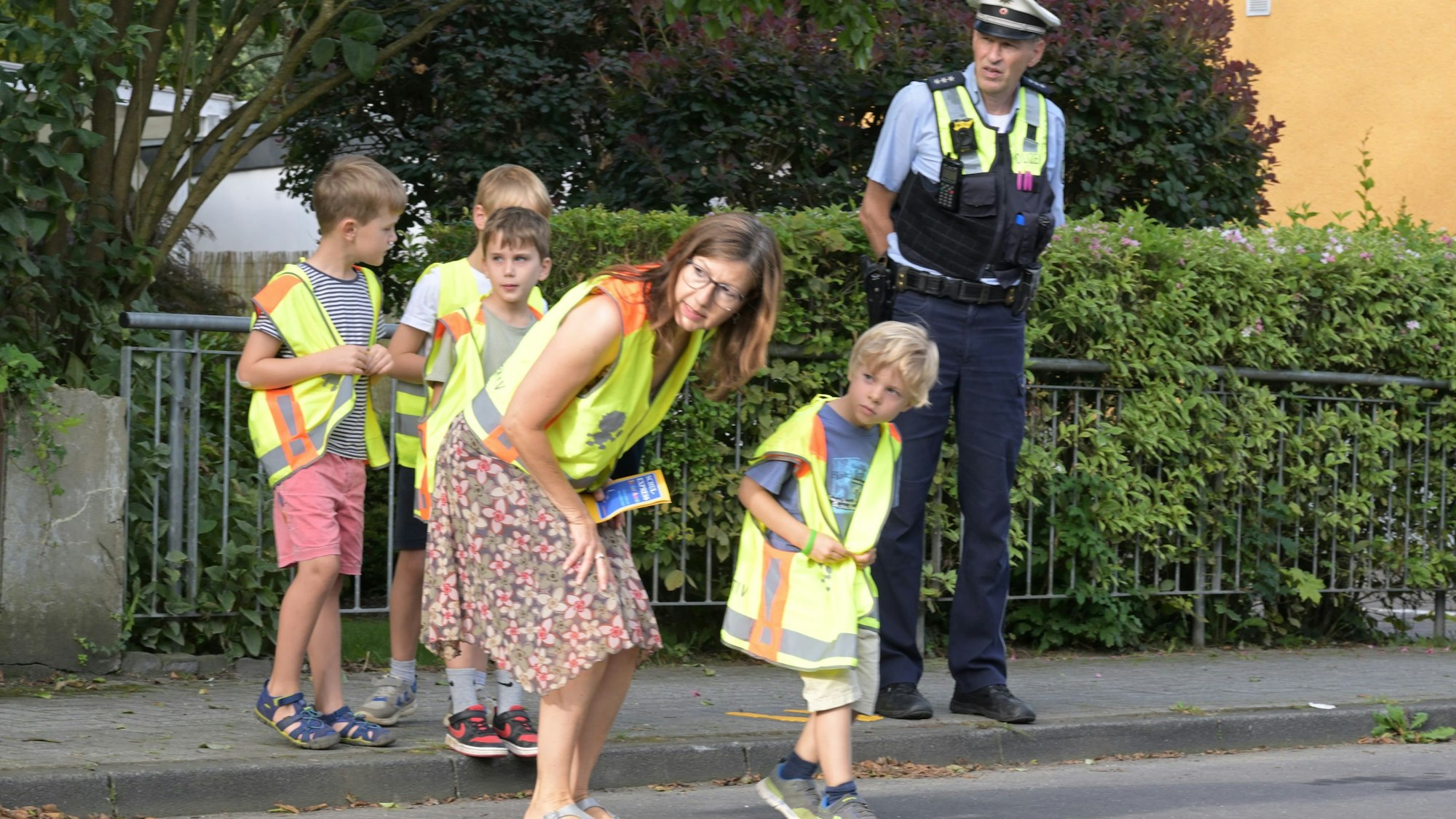 Eine Lehrerin und ein Polizist helfen Grundschülern über die Straße.