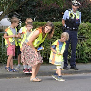 Eine Lehrerin und ein Polizist helfen Grundschülern über die Straße.&nbsp;