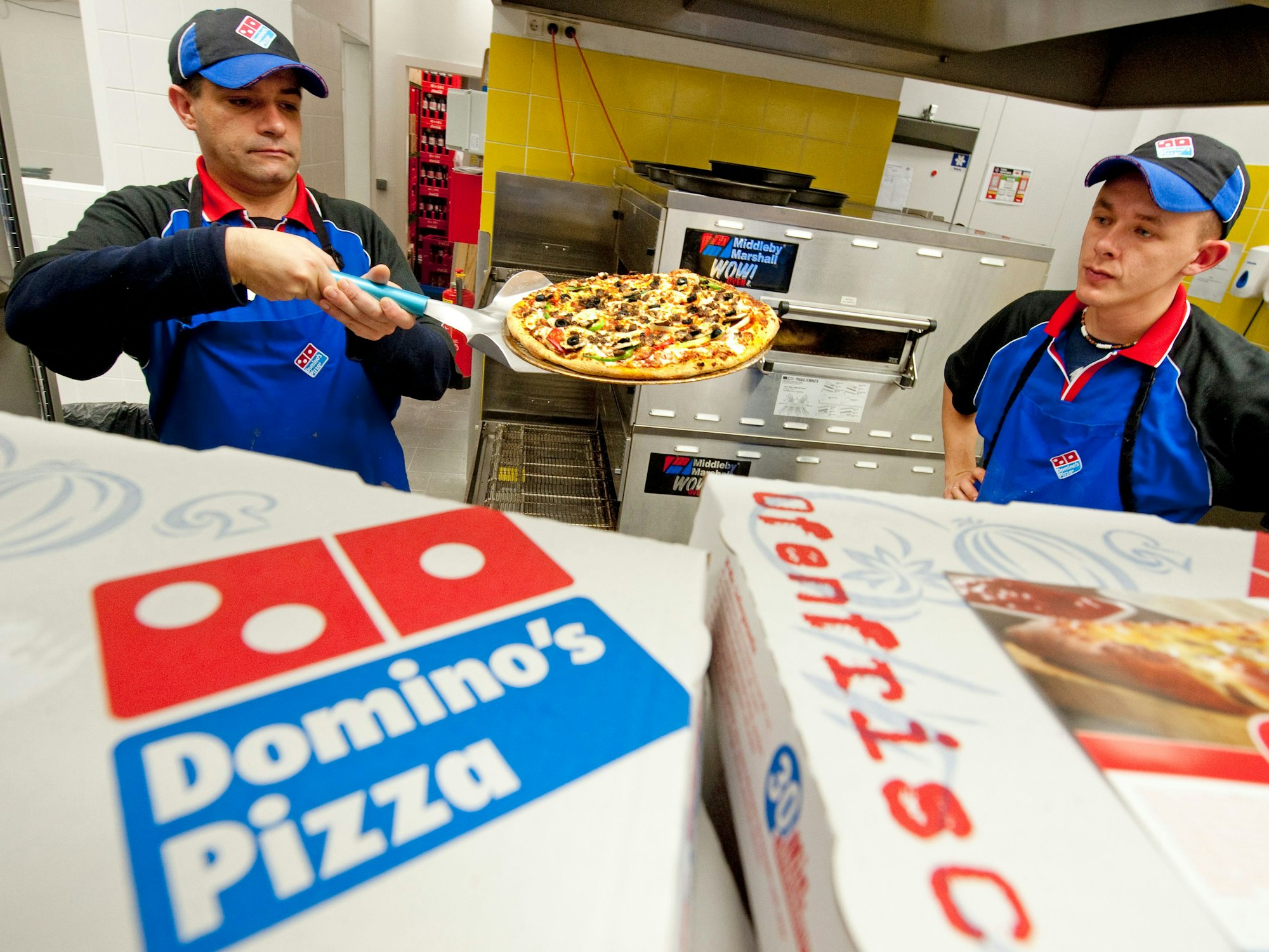 Ein Pizza-Bäcker von Domino's Pizza hält eine Pizza auf einem Pizza-Schieber in der Hand.