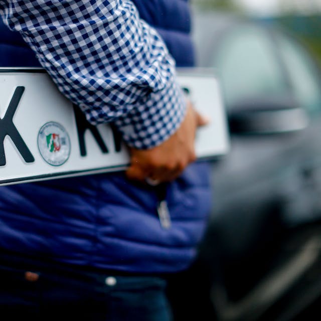 Ein Kunde trägt Nummernschilder vor der Kfz-Zulassungsstelle in Köln-Poll