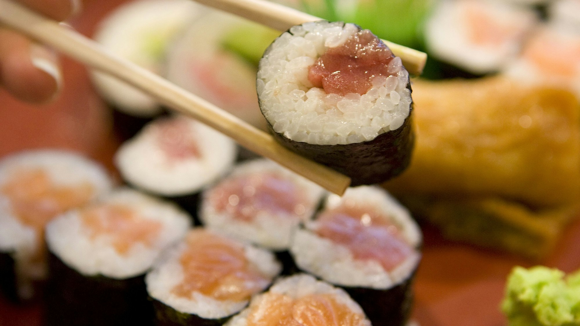 Ein Sushi Maki wird mit einem Stäbchen gehalten.