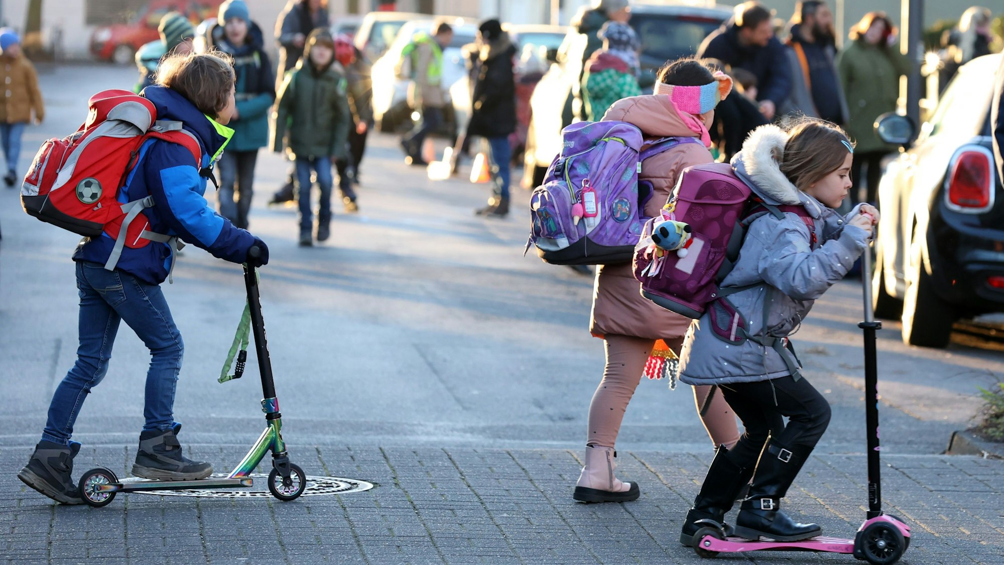 Schulkinder überqueren mit Roller und zu Fuß eine Straße