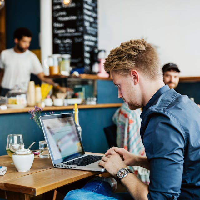 Ein junger Mann arbeitet in einem Café an seinem Laptop.