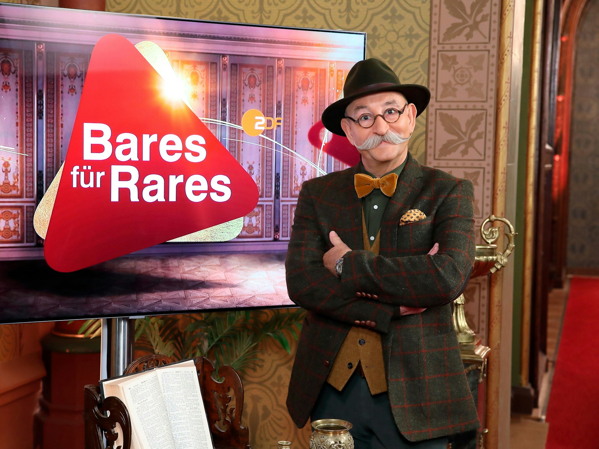 Moderator Horst Lichter steht neben dem Logo der Sendung „Bares für Rares“.
